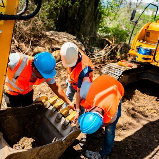 Construction workers inspecting an excavator bucket.